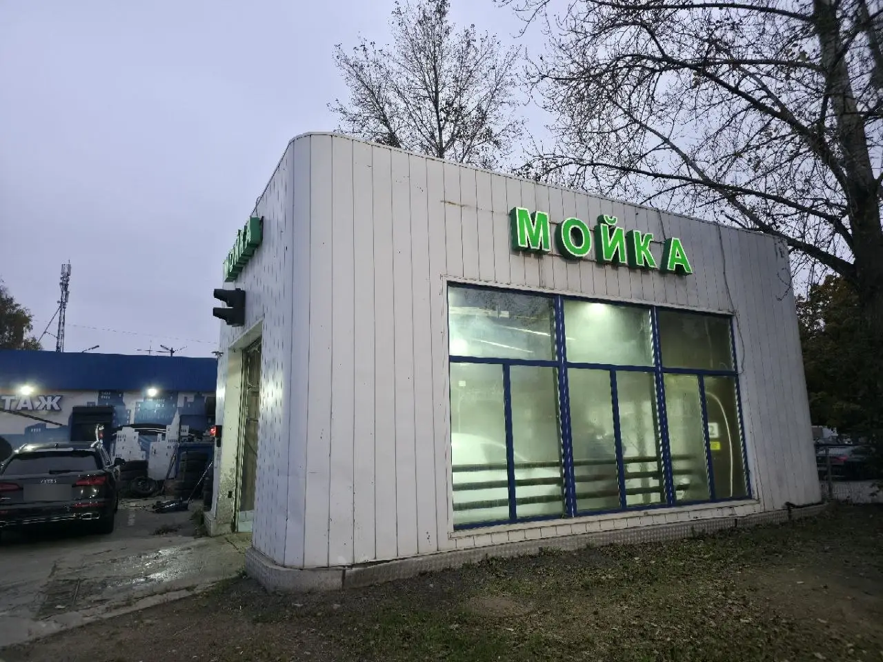 Здание мойки сбоку: белые стены, зелёная вывеска «МОЙКА», большие окна бокса